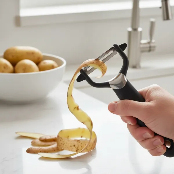 A close-up shot of an OXO Good Grips Pro Y-Peeler peeling a potato, showcasing its sharp blade and ergonomic handle.